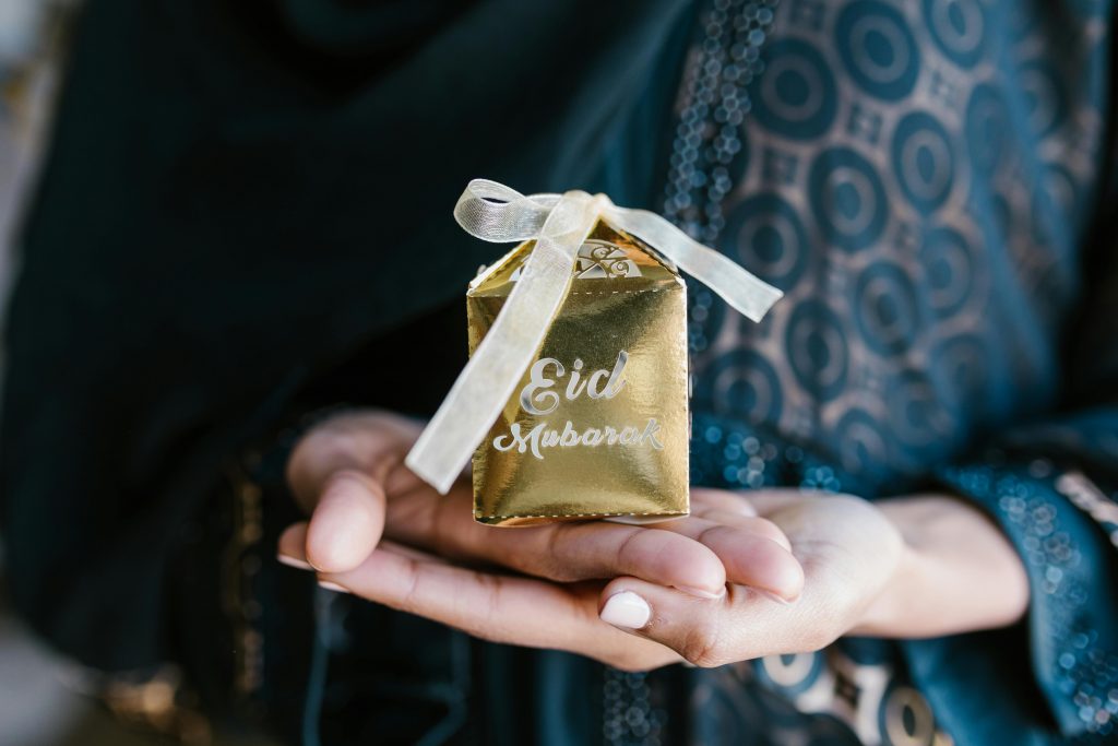 Gold gift box with ribbon and 'Eid Mubarak' text held in a woman's hand, perfect for festive greetings.